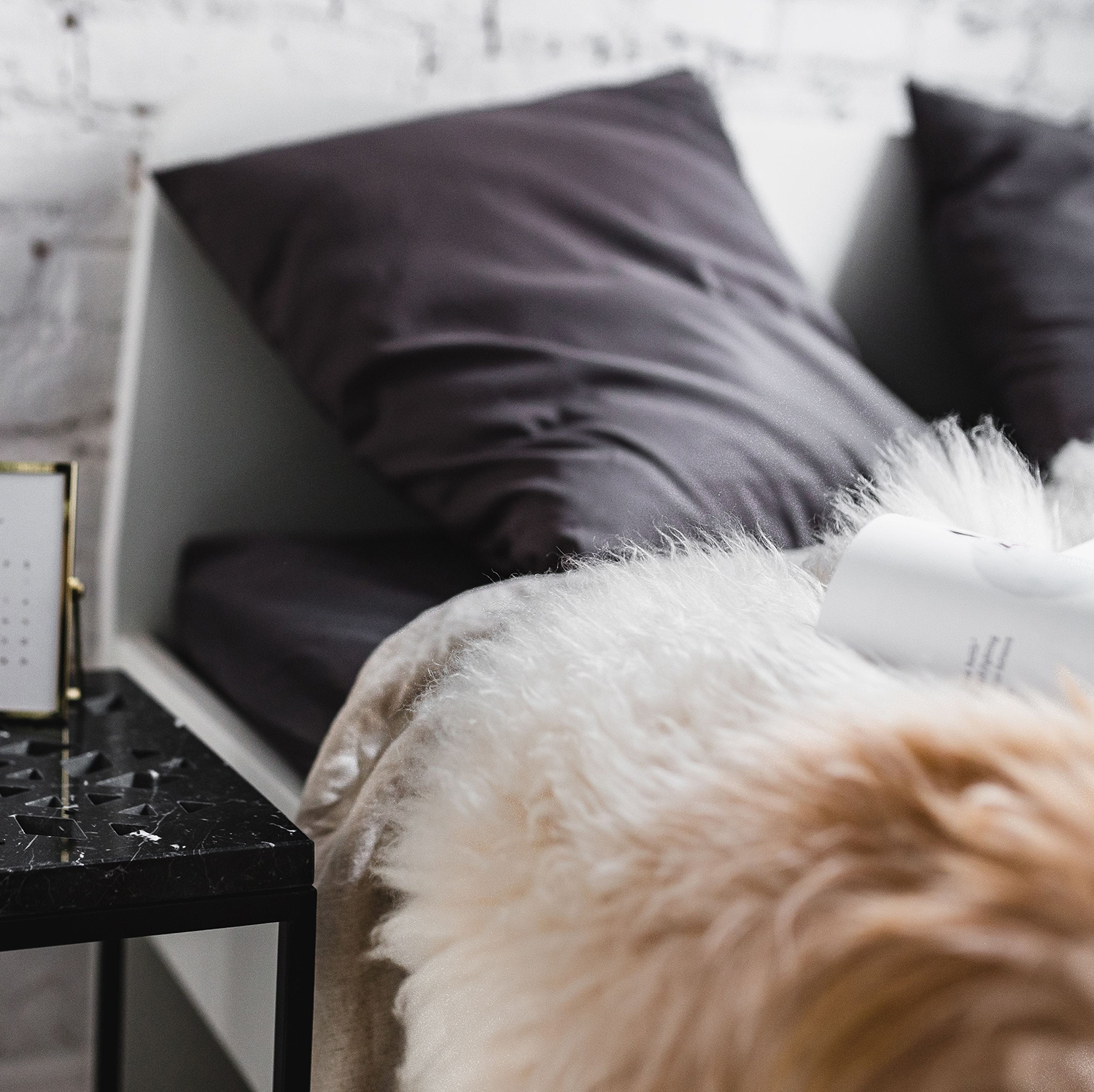 Détail du lit avec oreillers gris grahite et plaid fausse fourrure.