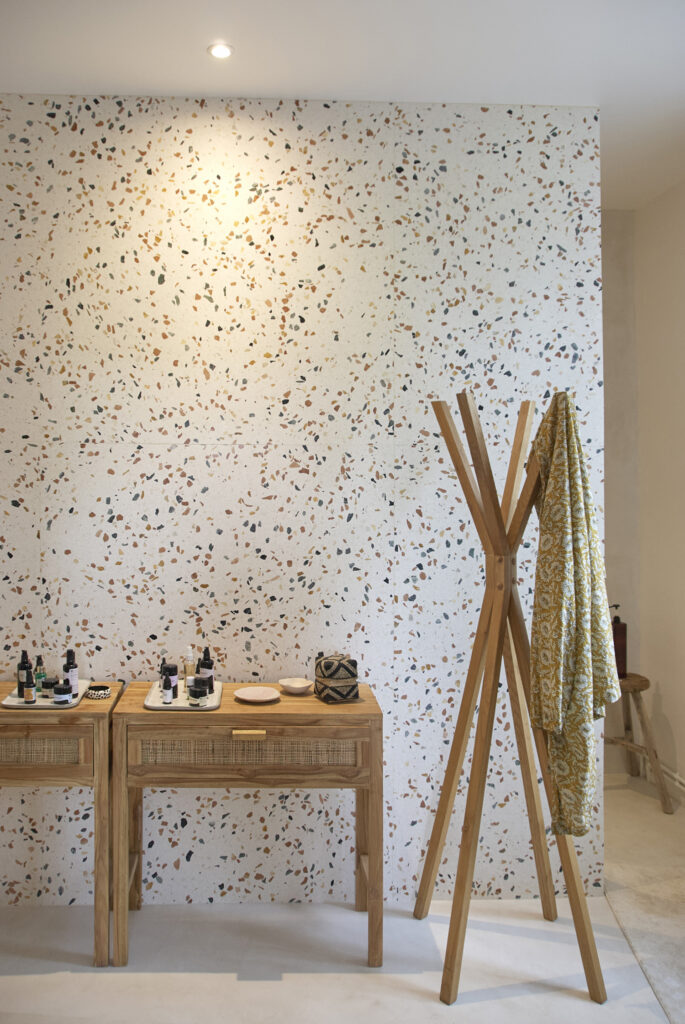 Mur en terrazzo associé au béton ciré du sol et de la douche, dans une salle de bain aux tons clairs.