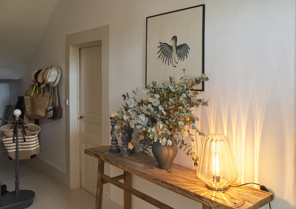 Hall d'entrée avec escalier en ferronnerie, avec console en bois brut, bouquet végétal aux nuances vert de gris et matières naturelles.