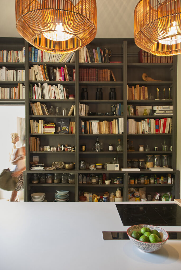 Cuisine avec bibliothèque intégrée, îlot central et suspension en fibres naturelles.