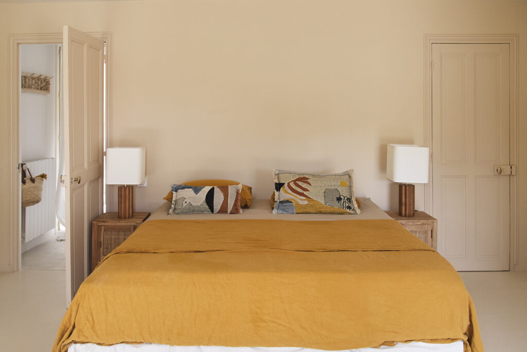 Chambre spacieuse avec portes anciennes, palette de teintes nude et linge de lit jaune safran.
