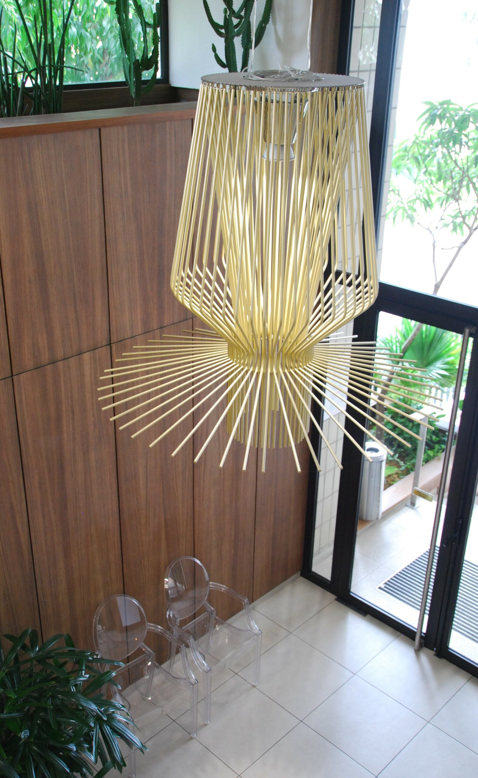 Vue plongeante sur le lustre Allegro Assaï Oro de Foscarini dans le hall d'accueil des salons VIP de l'aéroport international de Libreville. Placage mural en zébrano texturé et fauteuils "Ghost".