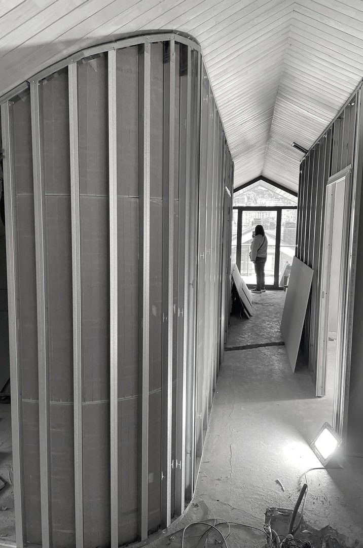 Vue du couloir en cours de transformation d'une penthouse, avec une cloison courbe en ossature métallique sous une toiture rampante.